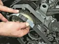 Hände montieren einen neuen Zahnriemen an einem Motor. So gelingt der Zahnriemenwechsel selbst.