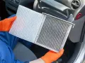 Person mit orangefarbenen Handschuhen hält einen neuen und einen schmutzigen Innenraumfilter. Zeit, den Innenraumfilter zu wechseln für saubere Luft im Auto.