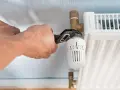 Hände wechseln einen Heizkörperthermostat mit einer Rohrzange.