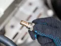 Defekte Lambdasonde als Ursache für die Motorkontrollleuchte. Ein Mechaniker hält das Bauteil in der Hand.