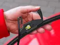 Hand wechselt Scheibenwischer an einem VW. Der Haken des Wischerarms wird in die Halterung eingeführt.