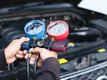 Hände halten ein Klimaanlagen-Manometer-Set, um den Druck zu prüfen. Dies ist ein Schritt zur Ermittlung der klimaanlage reparieren kosten.