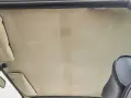 Der Dachhimmel kleben ist eine Kunst. Hier sieht man den hellen, gemusterten Dachhimmel eines Autos, mit Sonnenblenden und Rückspiegel.