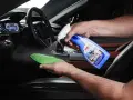 Mann sprüht Reinigungsmittel auf ein Mikrofasertuch, um Kunststoff im Auto zu reinigen.