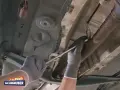Ein Mechaniker löst die Lambdasonde am Auspuffrohr. Sie sitzt im vorderen Teil des Rohrs, nahe am Motor.
