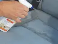 Hand sprüht Flecken aus Autositz mit Reiniger.