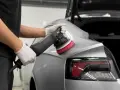 Detailarbeit beim **Lack polieren Auto**. Ein Mann mit Handschuhen nutzt eine Poliermaschine, um den glänzenden Lack auf Hochglanz zu bringen.