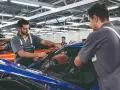 Zwei Mechaniker führen einen BMW Fahrzeugcheck durch. Einer entfernt die Windschutzscheibe, der andere sichert sie.