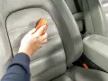 Hand reinigt grauen Leder-Autositz mit Bürste, um Wasserflecken zu entfernen.