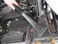 Hand saugt Laub und Schmutz aus dem Motorraum, um Feuchtigkeit im Auto vorzubeugen.