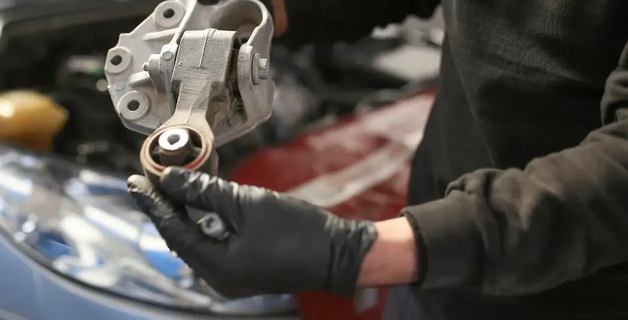 Mechaniker hält ein defektes Motorlager in der Hand, das ausgetauscht werden muss.