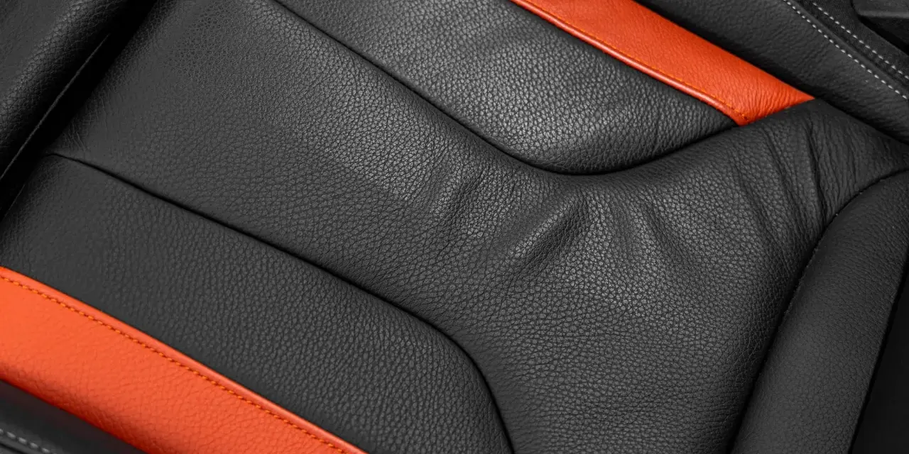 Detailaufnahme eines schwarzen Ledersitzes mit orangefarbenen Akzenten. Perfekt für die Leder reinigen Pflege.