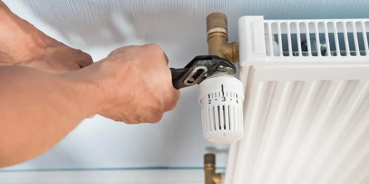Hände wechseln einen Heizkörperthermostat mit einer Rohrzange.