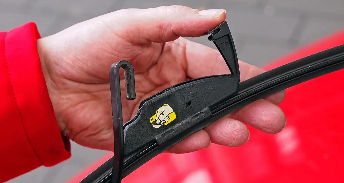 Hand wechselt Scheibenwischer an einem VW. Der Haken des Wischerarms wird in die Halterung eingeführt.