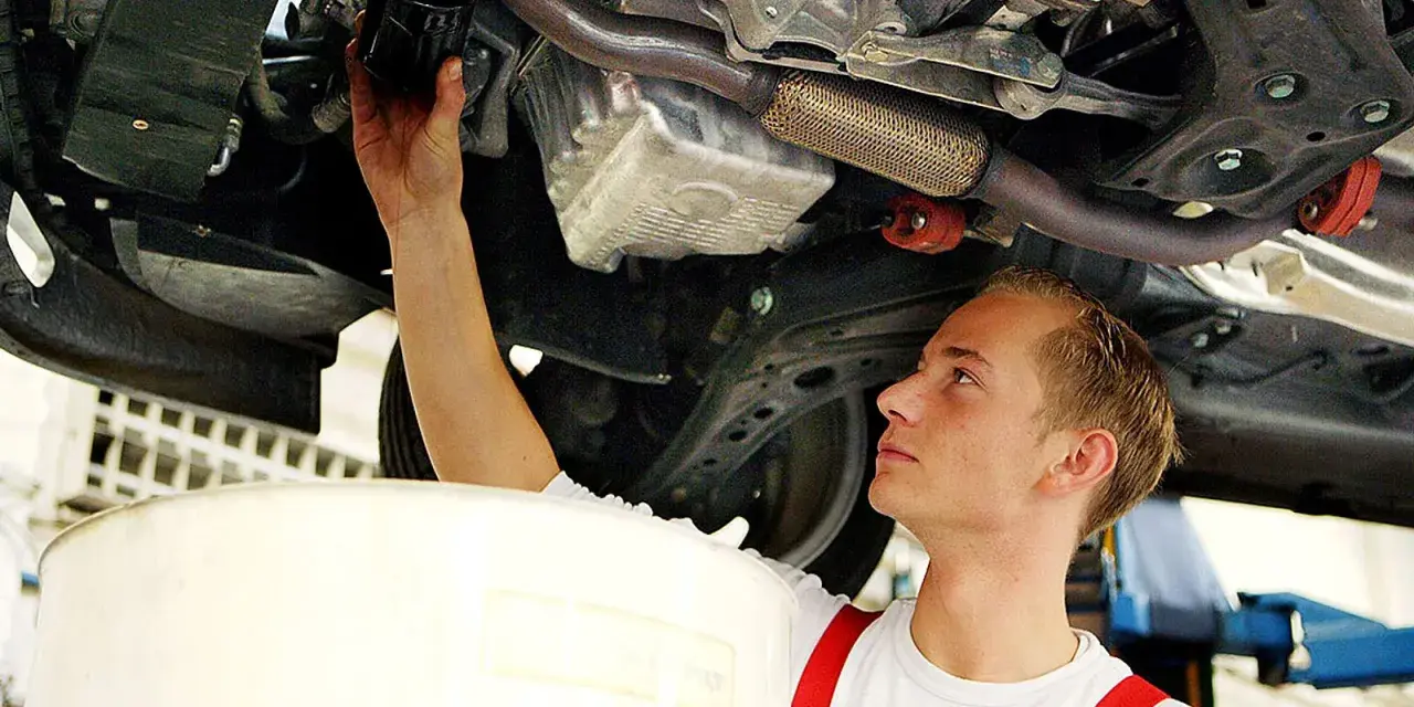 Ein junger Mechaniker bei einer Arbeitsstunde in der Kfz Werkstatt wechselt den Ölfilter unter einem Auto.