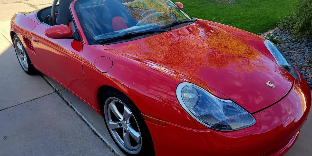 Roter Porsche Boxster Cabriolet. Die glänzende Karosserie spiegelt den Himmel wider. Ein Blick auf die potenziellen Porsche Service Kosten.