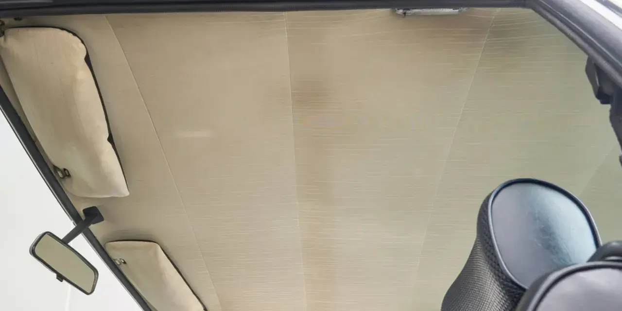Der Dachhimmel kleben ist eine Kunst. Hier sieht man den hellen, gemusterten Dachhimmel eines Autos, mit Sonnenblenden und Rückspiegel.