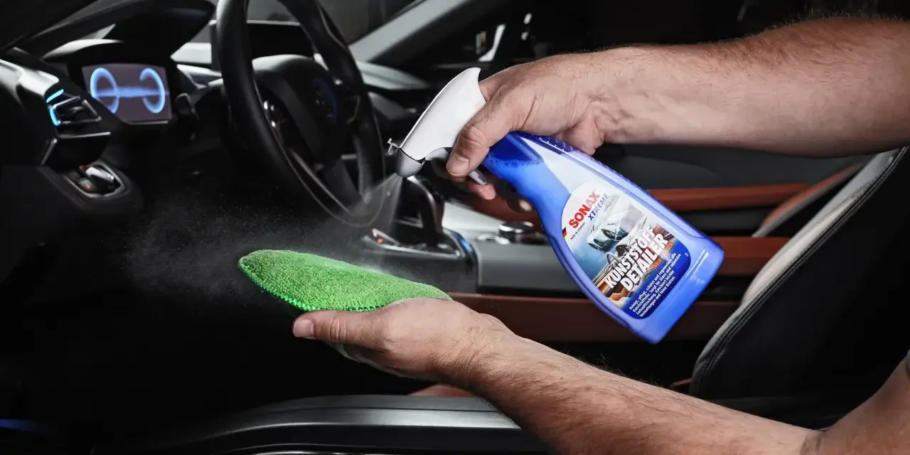 Mann sprüht Reinigungsmittel auf ein Mikrofasertuch, um Kunststoff im Auto zu reinigen.