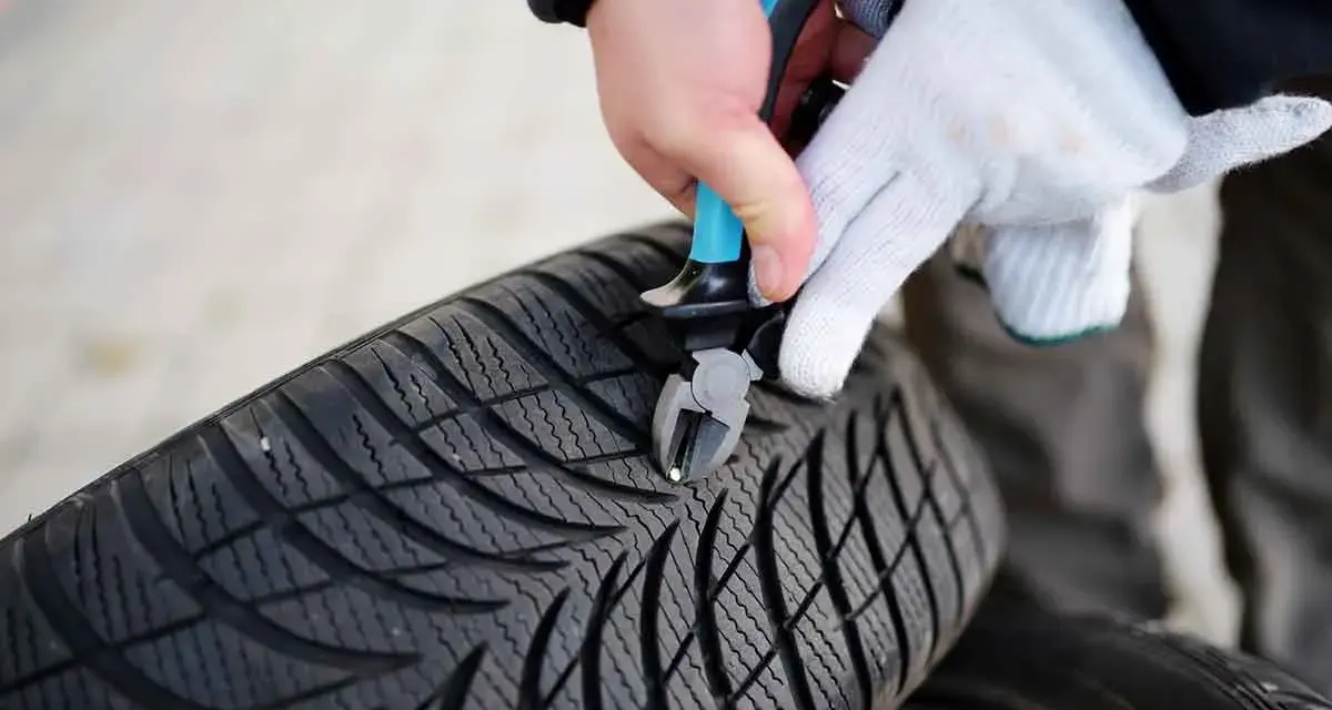Mit einer Zange wird ein kleiner Nagel aus dem Profil eines Autoreifens entfernt.
