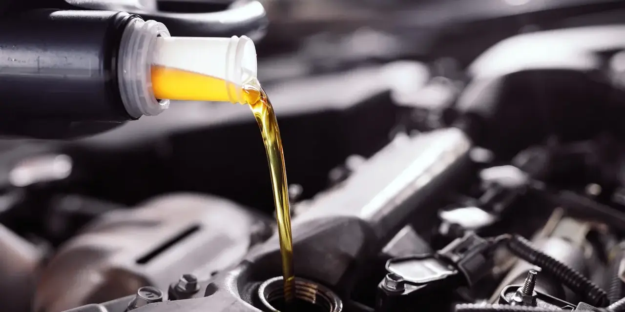 Frisches Öl fließt aus einer Flasche in einen Motor. Die API-Klassifikation des Öls ist entscheidend für die Leistung.