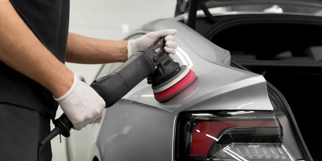 Detailarbeit beim **Lack polieren Auto**. Ein Mann mit Handschuhen nutzt eine Poliermaschine, um den glänzenden Lack auf Hochglanz zu bringen.