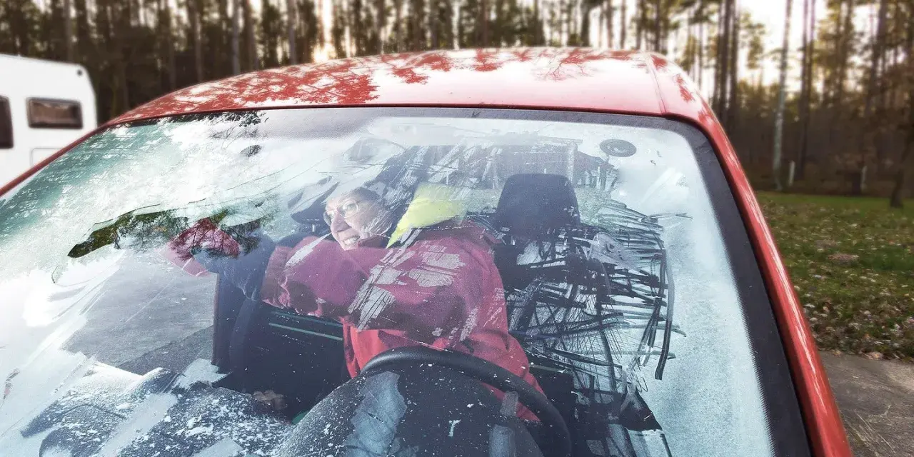 Frau versucht, die vereiste Autoscheibe innen freizukratzen. Tipps zur Vorbeugung von vereister Autoscheibe innen.