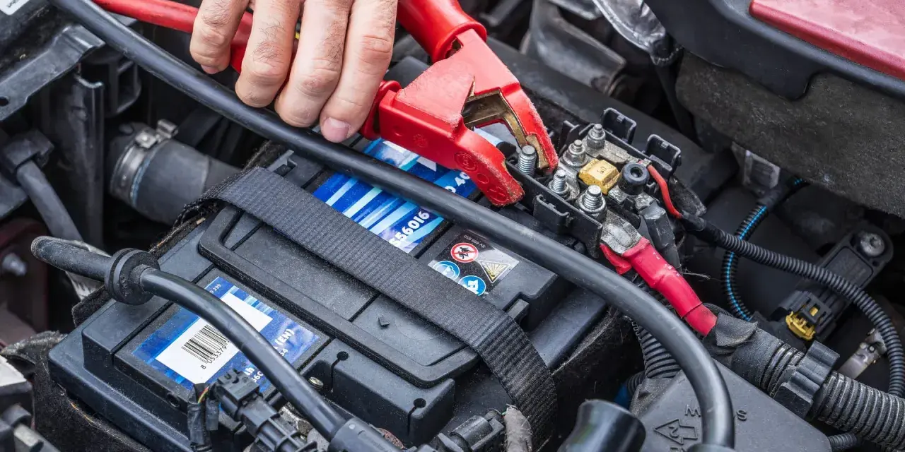 Starthilfe für eine leere Autobatterie: Rote und schwarze Klemmen werden an die Batterie angeschlossen.