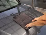 Hände trocknen das nasse Auto mit einem weichen auto trockentuch.
