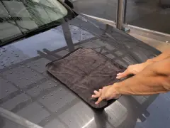 Hände trocknen das nasse Auto mit einem weichen auto trockentuch.