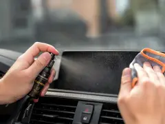 Mit einem Spray wird das Auto Display gereinigt. Eine Hand hält die Sprühflasche, die andere wischt mit einem Tuch über den Bildschirm.