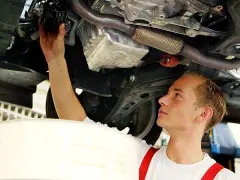 Ein junger Mechaniker bei einer Arbeitsstunde in der Kfz Werkstatt wechselt den Ölfilter unter einem Auto.