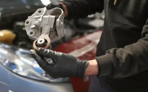 Mechaniker hält ein defektes Motorlager in der Hand, das ausgetauscht werden muss.