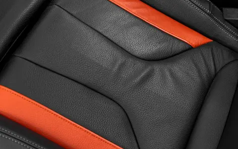 Detailaufnahme eines schwarzen Ledersitzes mit orangefarbenen Akzenten. Perfekt für die Leder reinigen Pflege.