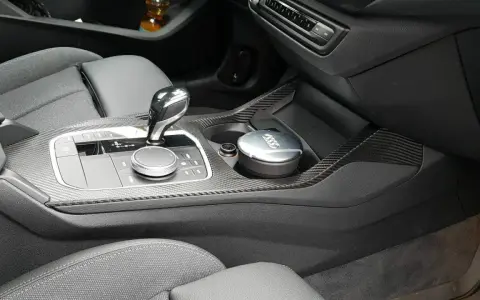 Detailaufnahme des Innenraums eines Autos mit Carbon-Akzenten. Ein Aschenbecher mit Audi-Logo steht im Getränkehalter. So reinigt man klavierlack auto.