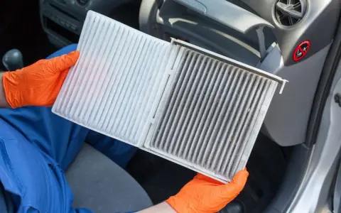 Person mit orangefarbenen Handschuhen hält einen neuen und einen schmutzigen Innenraumfilter. Zeit, den Innenraumfilter zu wechseln für saubere Luft im Auto.