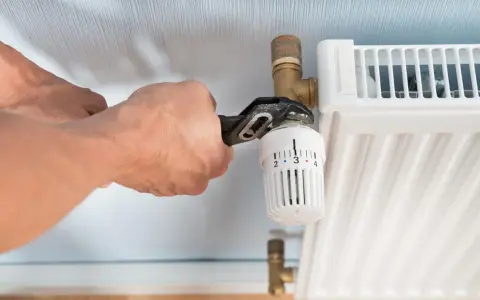 Hände wechseln einen Heizkörperthermostat mit einer Rohrzange.