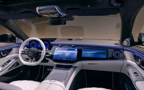 Luxuriöses Auto-Armaturenbrett mit großem Touchscreen, weißem Lenkrad und Ambientebeleuchtung.