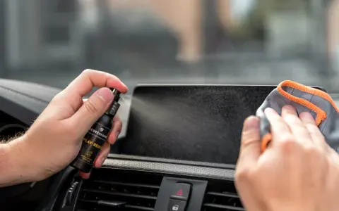 Mit einem Spray wird das Auto Display gereinigt. Eine Hand hält die Sprühflasche, die andere wischt mit einem Tuch über den Bildschirm.