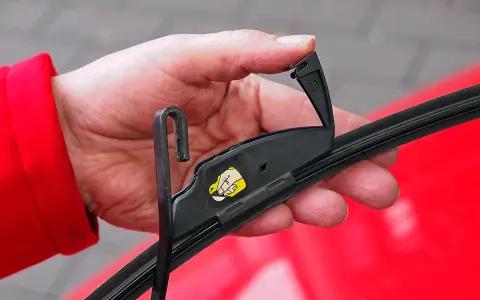Hand wechselt Scheibenwischer an einem VW. Der Haken des Wischerarms wird in die Halterung eingeführt.