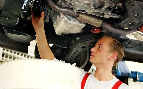 Ein junger Mechaniker bei einer Arbeitsstunde in der Kfz Werkstatt wechselt den Ölfilter unter einem Auto.