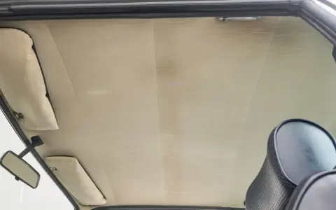 Der Dachhimmel kleben ist eine Kunst. Hier sieht man den hellen, gemusterten Dachhimmel eines Autos, mit Sonnenblenden und Rückspiegel.