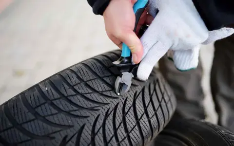 Mit einer Zange wird ein kleiner Nagel aus dem Profil eines Autoreifens entfernt.
