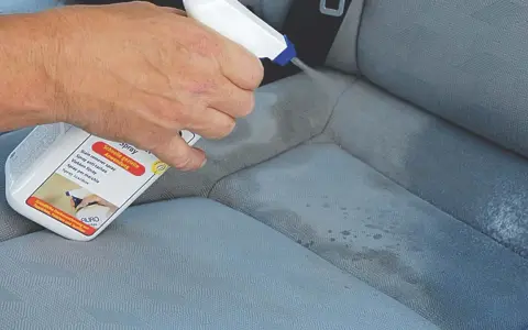 Hand sprüht Flecken aus Autositz mit Reiniger.