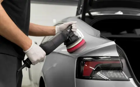 Detailarbeit beim **Lack polieren Auto**. Ein Mann mit Handschuhen nutzt eine Poliermaschine, um den glänzenden Lack auf Hochglanz zu bringen.