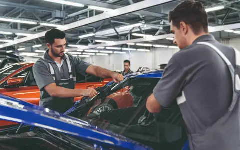 Zwei Mechaniker führen einen BMW Fahrzeugcheck durch. Einer entfernt die Windschutzscheibe, der andere sichert sie.