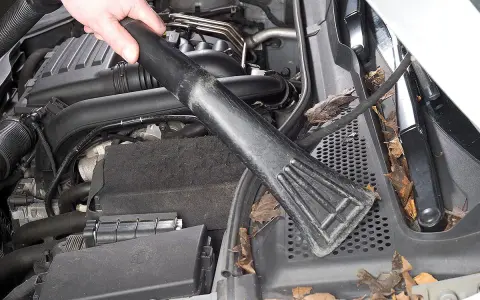 Hand saugt Laub und Schmutz aus dem Motorraum, um Feuchtigkeit im Auto vorzubeugen.
