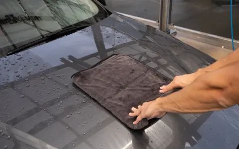 Hände trocknen mit einem Mikrofasertuch die Motorhaube nach der Autowäsche. Perfekt für das auto innenraum trocknen.