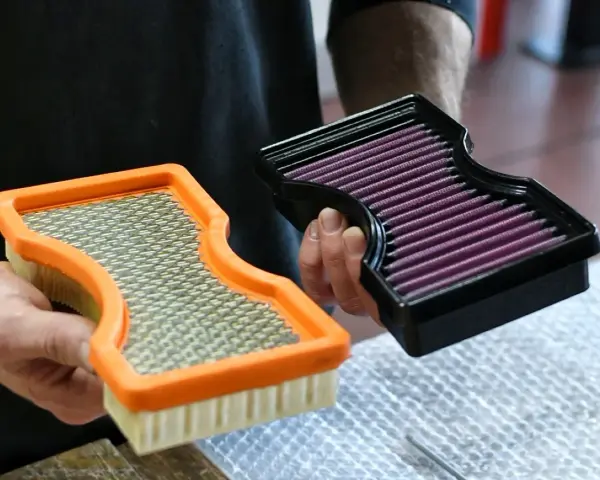 Hände halten zwei Luftfilter: einen orangen Standardfilter und einen schwarzen Sportluftfilter. Was bringt ein Sportluftfilter? Mehr Leistung!