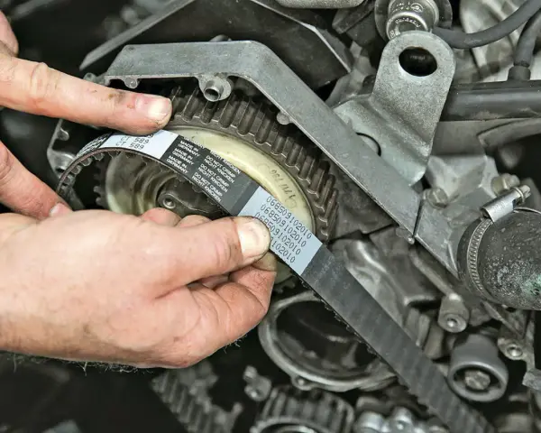 Hände montieren einen neuen Zahnriemen an einem Motor. So gelingt der Zahnriemenwechsel selbst.