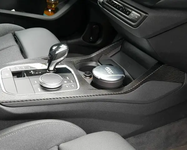 Detailaufnahme des Innenraums eines Autos mit Carbon-Akzenten. Ein Aschenbecher mit Audi-Logo steht im Getränkehalter. So reinigt man klavierlack auto.